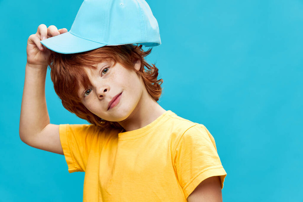 niño pelirrojo con una gorra en la cabeza fondo azul  - Foto, imagen