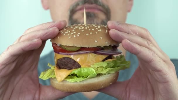 Bıyıklı ve sakallı bir adam hamburgeri elinde tutuyor ve inceliyor. - Video, Çekim