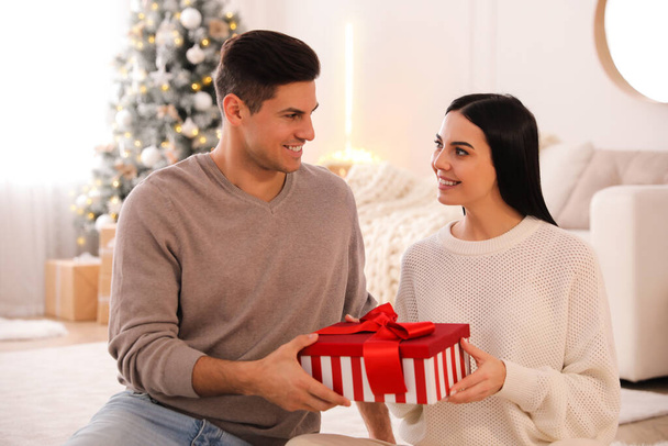 Couple holding gift box in room with Christmas tree - Foto, imagen
