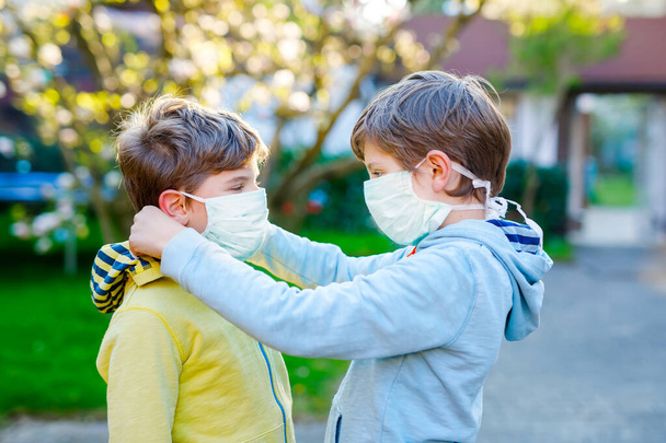 Kid boy helping brother to put medical mask on face as protection against pandemic coronavirus disease. Children, lovely siblings and best friends using protective equipment as fight against covid 19. - Φωτογραφία, εικόνα