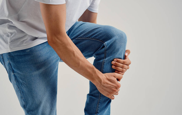 man in jeans touches his knee with his hands on a light background cropped view - Fotografie, Obrázek