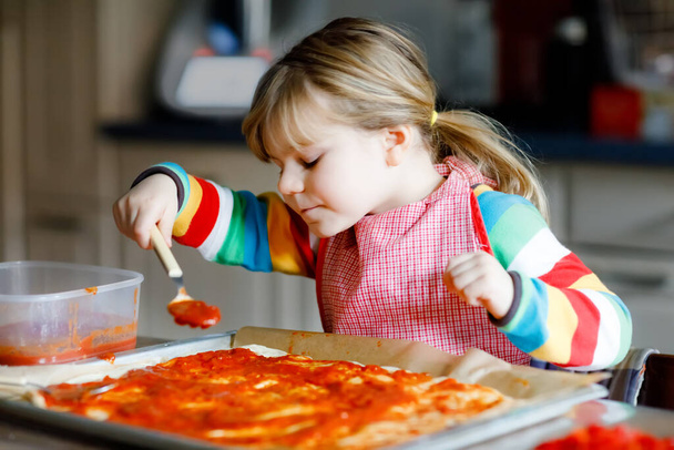 Adorable little toddler girl making italian pizza at home. Cute happy child having fun in home kitchen, indoors. Kid, preschooler helping and preparing healthy meal - Foto, Bild