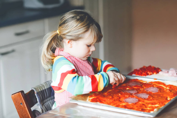 Imádnivaló kislány, aki olasz pizzát készít otthon. Aranyos boldog gyerek, aki otthon, a konyhában szórakozik. Kölyök, az óvodás segít és elkészíti az egészséges étkezést. - Fotó, kép
