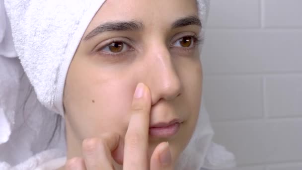 Girl without makeup in the bathroom. Black dots on the nose. A young woman looks at her face in the mirror. Skin care, problem skin, cleansing. Natural beauty, naturalness. Blackheads and comedones. - Footage, Video
