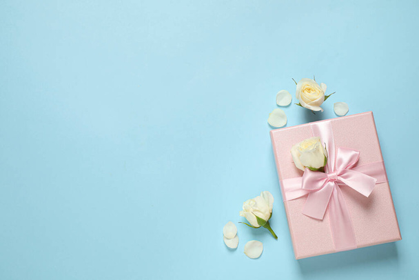 Pink gift box and beautiful flowers on light blue background, flat lay. Space for text - Foto, Bild