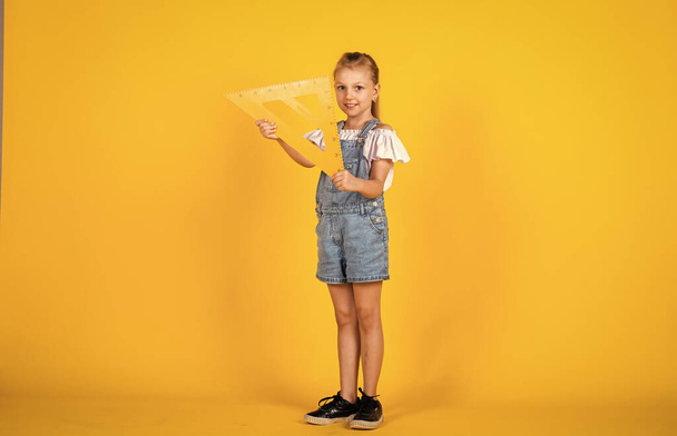 Education and school concept. small girl with triangle ruler. Math science concept with school lesson items. back to school. STEM school disciplines. Maths and geometry. what angle you look - Foto, afbeelding