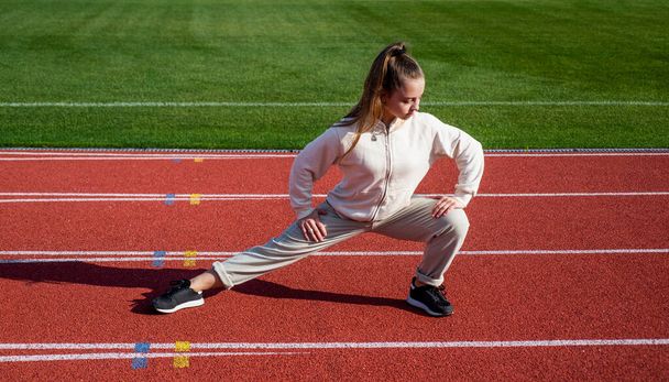 teen girl warming up on stadium. kid in sportswear stretching. child do exercise on racing track. healthy childhood. workout on fresh air outdoor. confident runner. flexible body - Fotó, kép