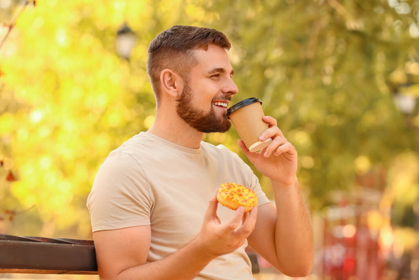 Joven guapo con rosquilla dulce y café en el parque - Foto, imagen