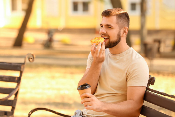 Handsome young man with sweet donut and coffee in park - Fotografie, Obrázek