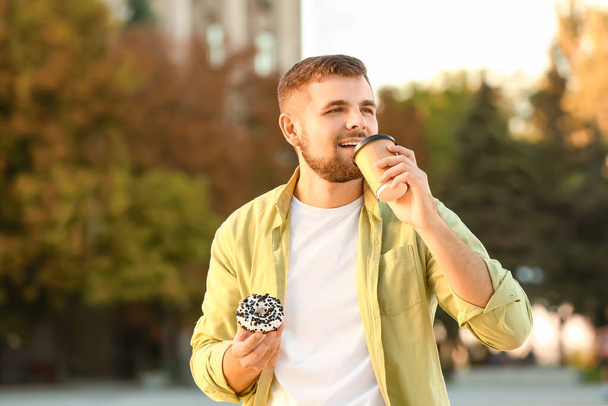 Handsome young man with sweet donut and coffee outdoors - Фото, зображення