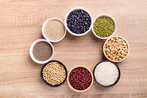 Vari cereali in una ciotola su fondo di legno (semi di quinoa, fagioli neri, arachidi, semi di perilla, soia, fagioli azuki, riso e fagioli mung) - Foto, immagini