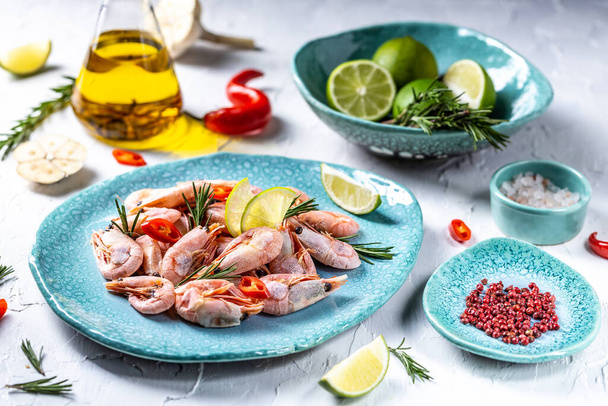 Gekochte Garnelen serviert mit Limette, Rosmarin, Chili auf einem blauen Teller, Meeresfrüchte. - Foto, Bild