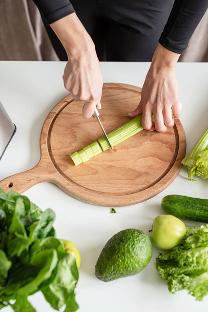 Healthy eating, dieting concept. High angle view of female hands cutting celery in the kitchen - Foto, Imagen