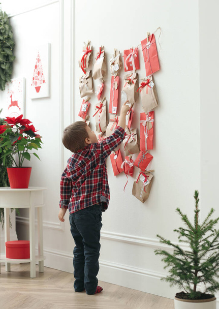Cute little boy taking gift from Advent calendar at home. Christmas tradition - Fotó, kép