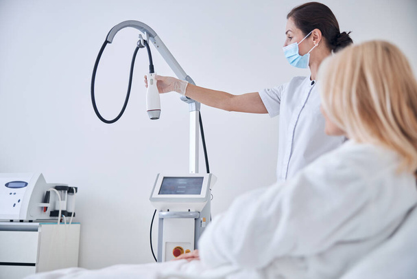 Esthéticienne faisant la démonstration d'une nouvelle machine à ultrasons pour éplucher le visage - Photo, image
