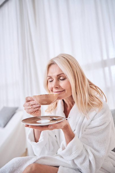Relaxed blonde Caucasian woman enjoying tasty cup of tea in spa salon - Fotoğraf, Görsel
