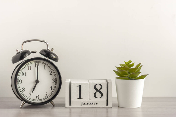18. Januar auf einem hölzernen Kalender, neben einem Retro-Wecker und einer Sukkulente in einem Mini-Topf auf einem hellen Tisch. Ein Januartag. Wintertag.Eine Kopie des Raum.Arbeitsplatz. - Foto, Bild