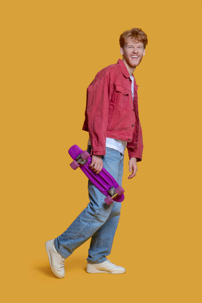 Man in red jacket holding a skateboard and smiling - Zdjęcie, obraz