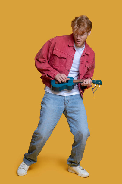 Man in red jacket playing the ukulele - Photo, image