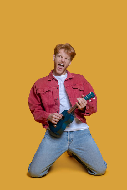 Man in red jacket playing the ukulele and looking enjoyed - Photo, image