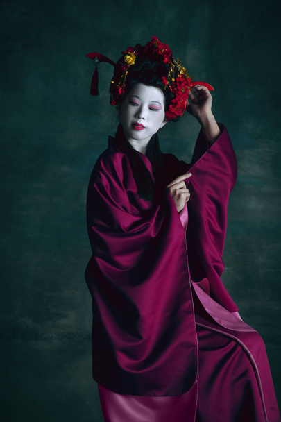 Young japanese woman as geisha on dark green background. Retro style, comparison of eras concept. - Photo, image