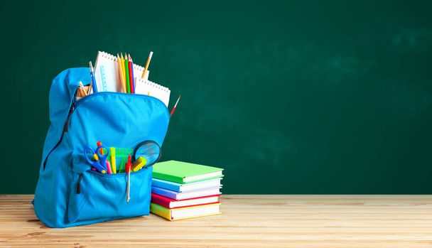 School bag. Backpack with supplies for school on the background of green blackboard. Copy space for text. - Foto, Imagen