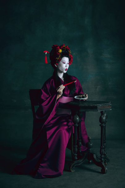 Молодая японская женщина в роли гейши на темно-зеленом фоне. Ретро стиль, сравнение эпох концепции. - Фото, изображение