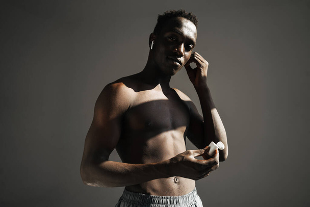 Pleased african american sportsman using earphones while working out isolated over grey background - Fotó, kép