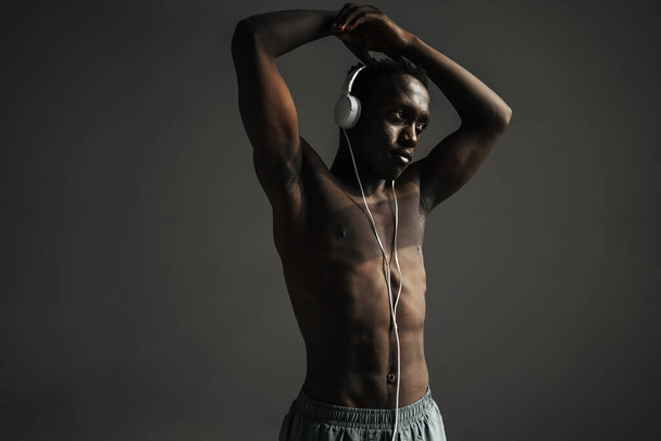 Shirtless african american sportsman using headphones while stretching his arm isolated over grey background - Valokuva, kuva