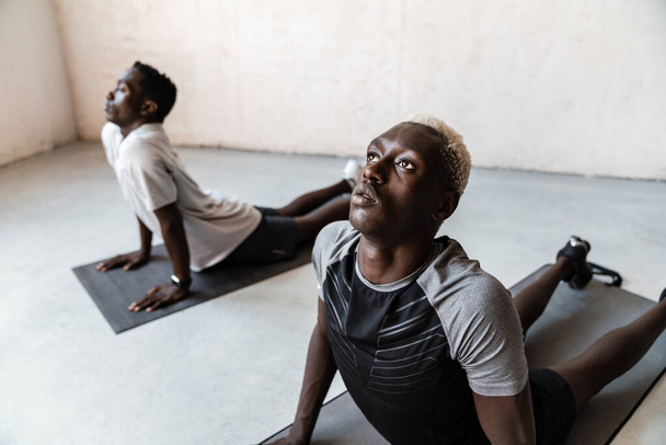 Two young athletic african american men doing workout on exercise mat indoors - Fotoğraf, Görsel