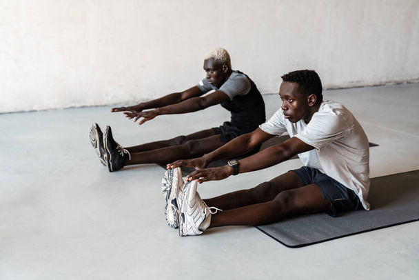Двоє молодих атлетичних афроамериканських чоловіків займаються спортом на маті в приміщенні. - Фото, зображення