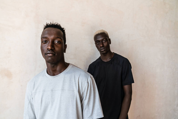 Two young handsome african american men looking at camera while standing over wall indoors - Фото, зображення