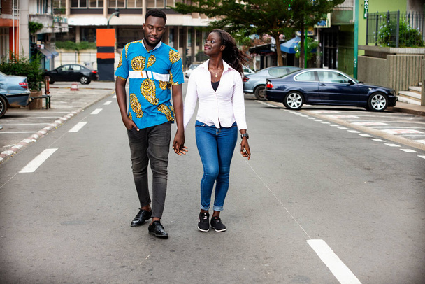 Young african couple talking while walking hand in hand outdoors in the street smiling, love story - Fotó, kép