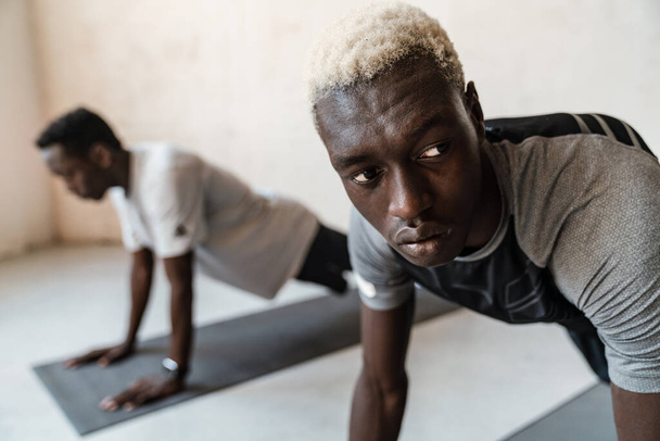 Two young handsome african american men stretching their bodies while doing workout indoors - Fotografie, Obrázek
