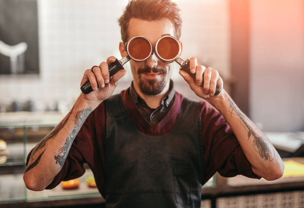 Hipster barista covering eyes with portafilters - Foto, Imagem