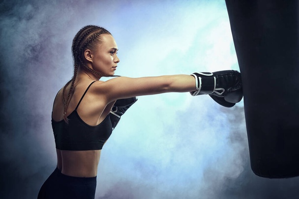 woman in boxing gloves and sportswear kicking bag - Foto, Bild