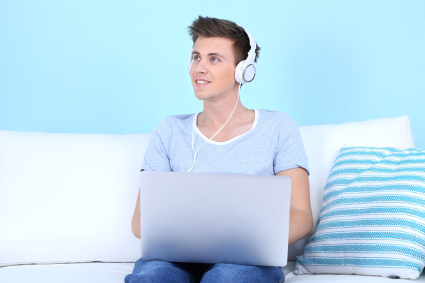 Guy sitting on sofa and  listening to music on blue background - Zdjęcie, obraz