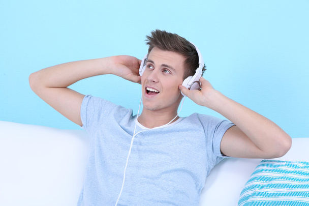Guy sitting on sofa and  listening to music on blue background - Foto, Imagen