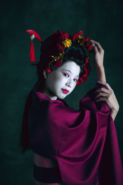 Young japanese woman as geisha on dark green background. Retro style, comparison of eras concept. - Fotó, kép