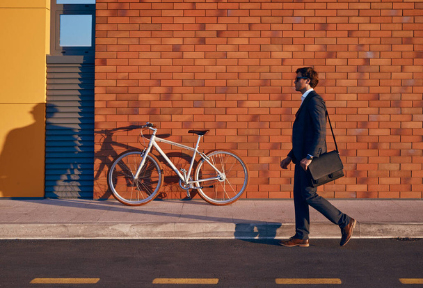 Male entrepreneur walking on road near bicycle - Zdjęcie, obraz