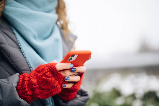 Zbliżenie kobieta ręka smsuję na smartfon, stojąc na ulica w zimowy miasto na nowy rok. Kobiece palce stukające komórką na zewnątrz. Nowoczesne wakacje zakupy online, kupowanie prezentów noworocznych - Zdjęcie, obraz