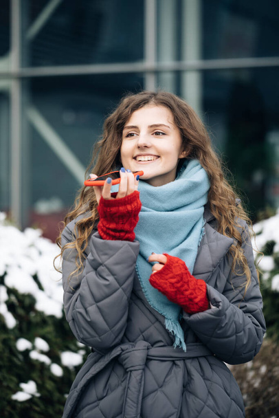 Portrait of Curly-haired Woman with phone using the voice recognition ai audio message on the phone, audio message ai speech helper. Vacation winter outdoor - Fotoğraf, Görsel