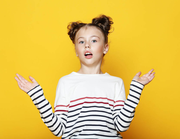 Portrait of cheerful surprised little girl on yellow background - Photo, Image