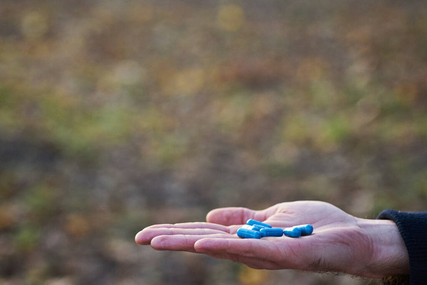 Close up of male hands with blue pills in hand. Natural background. Cure concept. - Photo, Image