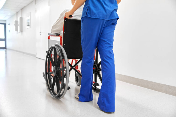 νοσοκόμα με ηλικιωμένο ασθενή σε αναπηρική καρέκλα στην κλινική - Φωτογραφία, εικόνα
