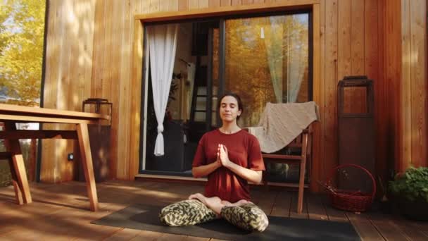 Tilt down shot of young relaxed woman meditating in lotus pose with eyes closed, holding hands in prayer position and then in mudras while practice yoga on outdoor terrace - Imágenes, Vídeo