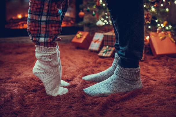 Woman feet standing in tip toe in winter socks near male lags on a fluffy red blanket near a Christmas tree with gifts. Concept  - Photo, Image