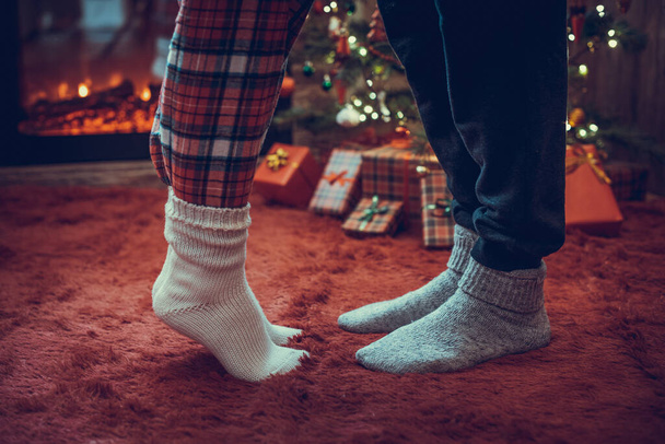 Woman feet standing in tip toe in winter socks near male lags on a fluffy red blanket near a Christmas tree with gifts. Concept  - Photo, image