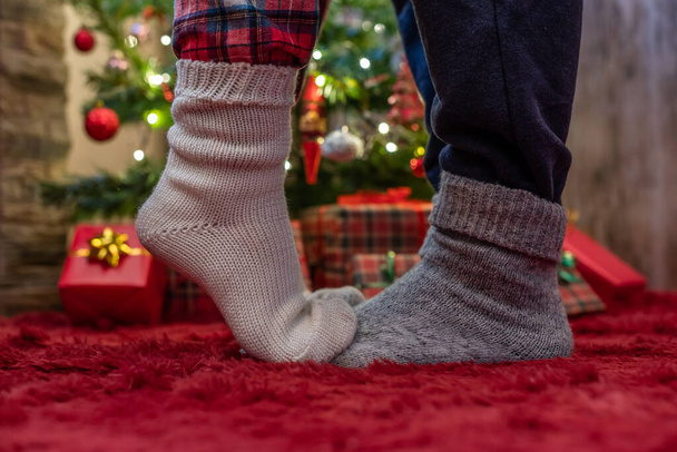 Woman feet standing in tip toe in winter socks on male lags on a fluffy red blanket near a Christmas tree with gifts. Concept  - Valokuva, kuva