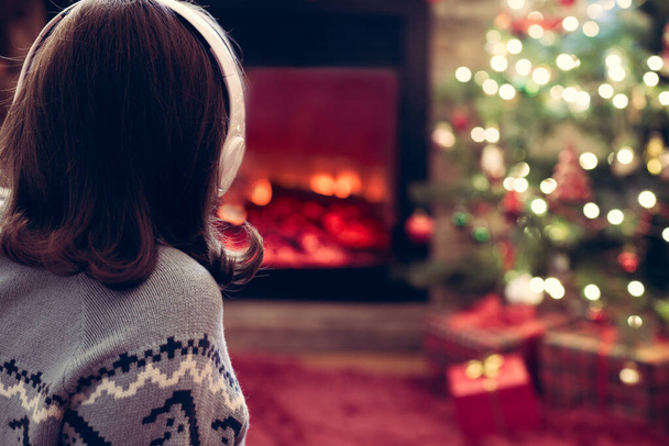 Woman in headphones sitting and warming at winter evening near fireplace flame and  christmas tree. - Zdjęcie, obraz